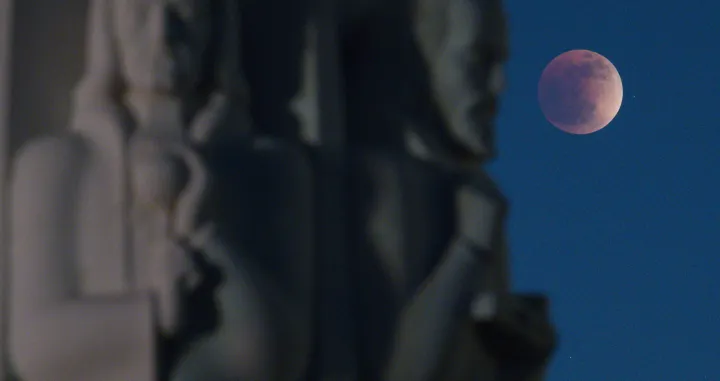 epa09950171 The Super Flower Blood Moon lunar eclipse peers behind the 'Astronomers Monument', including statues of Johanees Kepler (R) and Isaac Newton (L), at the Griffith Observatory in Los Angeles, California, USA, 15 May 2022. EPA/CAROLINE BREHMAN/Caroline Brehman