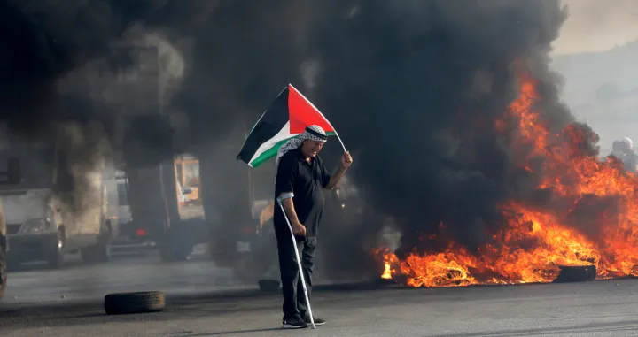 epa09984901 A Palestinian waves Palestine flag during clashes with Israeli troops near Huwwara checkpoint in the West Bank city of Nablus, 29 May 2022. According to Palestinian medical sources, 70 Palestinians were wounded during the clashes after protests against the Israeli 'Flags March'. EPA/ALAA BADARNEH/Alaa Badarneh