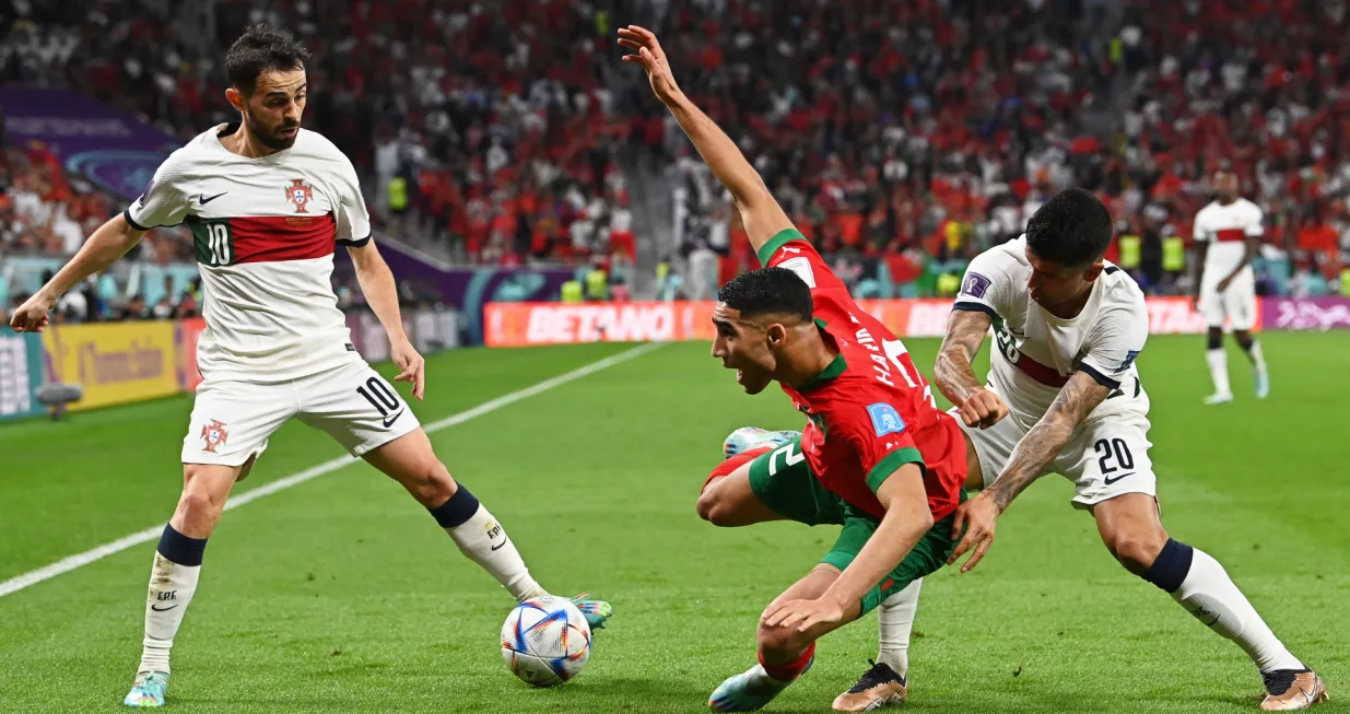 epa10359586 Achraf Hakimi (C) of Morocco in action against Portuguese players Bernardo Silva (L) and Joao Cancelo (R) during the FIFA World Cup 2022 quarter final soccer match between Morocco and Portugal at Al Thumama Stadium in Doha, Qatar, 10 December 2022. EPA/Georgi Licovski