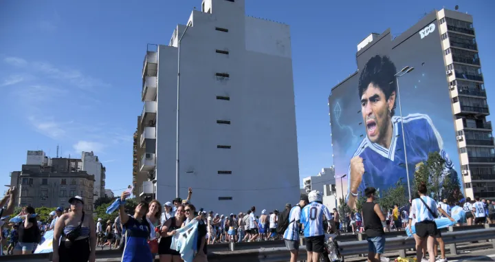 epa10375178 Fans of Argentinian national soccer team celebrate during the victory parade of the Argentinian national soccer team in Buenos Aires, Argentina, 20 December 2022 as a mural depicting soccer legend Diego Maradona of Argentina is seen. Argentina defeated France 4-2 in a penalty shoot-out after a 3-3 draw to win the FIFA World Cup 2022 soccer tournament. The parade was stopped early because the streets were overflowing with fans and the Argentine team had to return to the sports venue of the Argentine Football Association (AFA) located in Ezeiza by helicopter. EPA/Enrique García Medina