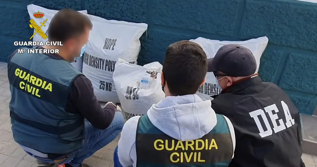epa09765343 An undated handout photo made available by the Spanish Civil Guard on 17 February 2022 shows two Spanish Civil Guard officers and a US Drug Enforcement Agency (DEA)'s agent looking at sacks containing cocaine hidden among colorful polyethylene terephthalate (PET) flakes during an international police operation against drug trafficking, in Alicante, Spain. A total of 18 people were arrested and over 1,000 kilograms of cocaine were seized in the joint operation carried out by the Civil Guard, the DEA, Colombia's anti-narcotics police (DIRAN), and the Ecuadorian Police. EPA/Spanish Civil Guard HANDOUT IMAGE BLURRED AT SOURCE HANDOUT EDITORIAL USE ONLY/NO SALES/Spanish Civil Guard Handout
