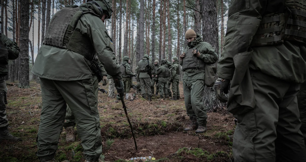 A Lithuanian instructor uses a tree branch as a pointer to demonstrate a plan, while Ukrainian soldiers observe./Nato