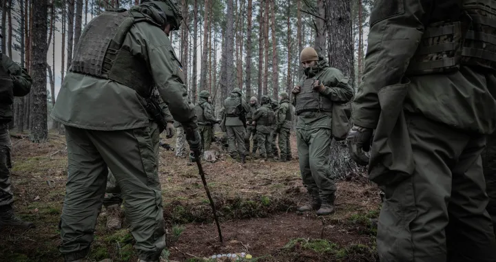 A Lithuanian instructor uses a tree branch as a pointer to demonstrate a plan, while Ukrainian soldiers observe./Nato