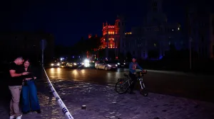 People check their mobile phones near the town hall building at Cibeles Square as some lights begin to come back on during a nationwide power outage in Madrid, Spain, April 28, 2025. REUTERS/Susana Vera/Susana Vera