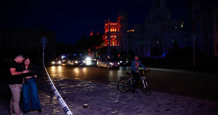 People check their mobile phones near the town hall building at Cibeles Square as some lights begin to come back on during a nationwide power outage in Madrid, Spain, April 28, 2025. REUTERS/Susana Vera/Susana Vera