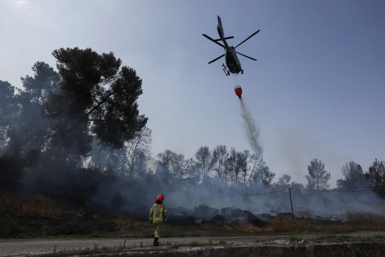 A firefighter walks as a helicopter drops water, a day after wildfires broke out due to extreme heat and winds, in Latrun, central Israel, May 1, 2025. REUTERS/Ronen Zvulun/Ronen Zvulun