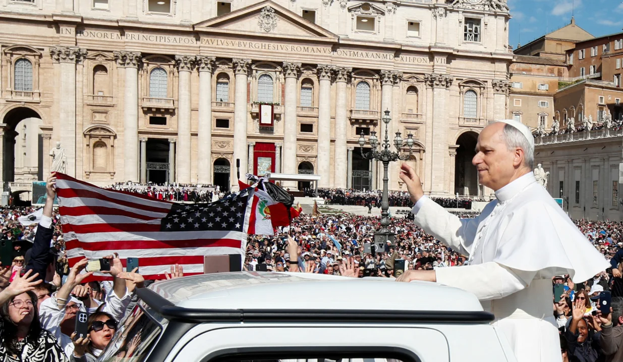 A U.S. flag is held up as Pope Leo XIV waves to the faithful from the popemobile ahead of his inaugural Mass in Saint Peter's Square, at the Vatican, May 18, 2025. REUTERS/Alessandro Garofalo/Alessandro Garofalo