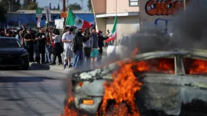 Protesters stand near a car burning in flames following multiple detentions by Immigration and Customs Enforcement (ICE), in the Los Angeles County city of Paramount, California, U.S., June 7, 2025. REUTERS/Daniel Cole/Daniel Cole