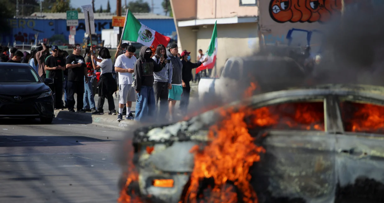 Protesters stand near a car burning in flames following multiple detentions by Immigration and Customs Enforcement (ICE), in the Los Angeles County city of Paramount, California, U.S., June 7, 2025. REUTERS/Daniel Cole/Daniel Cole
