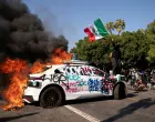 FILE PHOTO: SENSITIVE MATERIAL. THIS IMAGE MAY OFFEND OR DISTURB A person waves a Mexican flag atop a burning vehicle during a protest against federal immigration sweeps in downtown Los Angeles, California, U.S. June 8, 2025. REUTERS/David Ryder/File Photo/David Ryder
