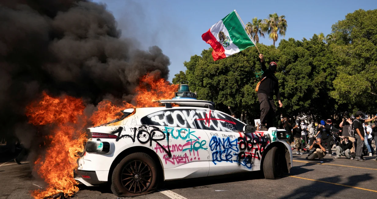 FILE PHOTO: SENSITIVE MATERIAL. THIS IMAGE MAY OFFEND OR DISTURB A person waves a Mexican flag atop a burning vehicle during a protest against federal immigration sweeps in downtown Los Angeles, California, U.S. June 8, 2025. REUTERS/David Ryder/File Photo/David Ryder