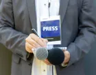 Male journalist at news conference or media event, holding microphone, writing notes. Journalism concept./