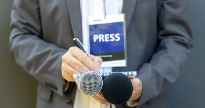 Male journalist at news conference or media event, holding microphone, writing notes. Journalism concept./