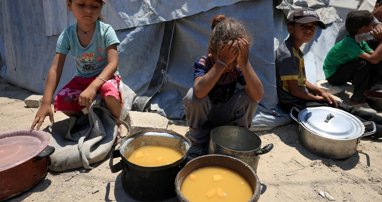 Palestinian children react near pots of food from a charity kitchen, amid a hunger crisis, in Gaza City, July 25, 2025. REUTERS/Dawoud Abu Alkas/Dawoud Abu Alkas