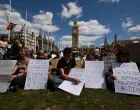 People holding signs sit during a rally organised by Defend Our Juries, challenging the British government's proscription of "Palestine Action" under anti-terrorism laws, in Parliament Square, in London, Britain, August 9, 2025. REUTERS/Jaimi Joy/Jaimi Joy