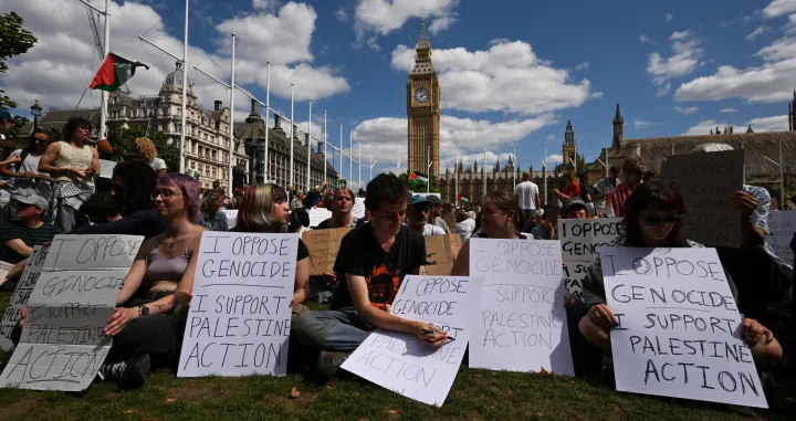 People holding signs sit during a rally organised by Defend Our Juries, challenging the British government's proscription of "Palestine Action" under anti-terrorism laws, in Parliament Square, in London, Britain, August 9, 2025. REUTERS/Jaimi Joy/Jaimi Joy