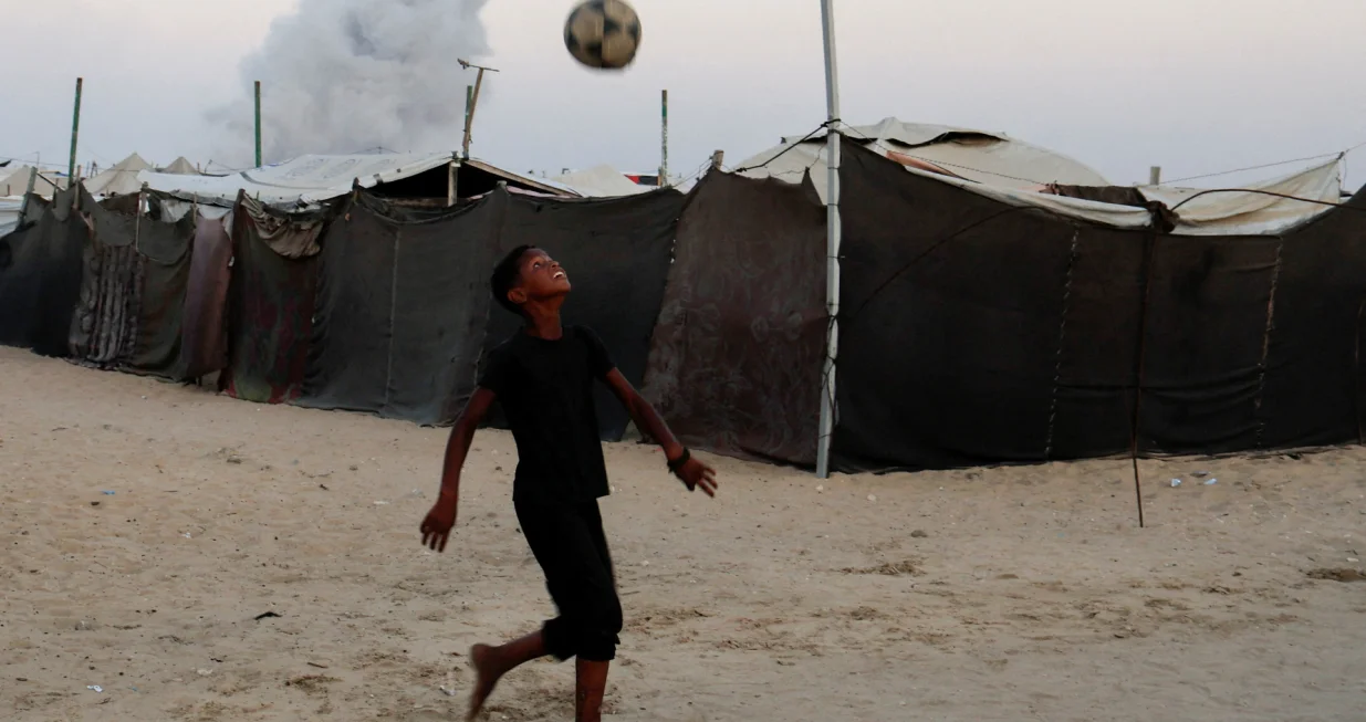 Palestinski dječak igra fudbal dok se dim diže nakon izraelskog napada u Khan Younisu/REUTERS/Foto: Hatem Khaled