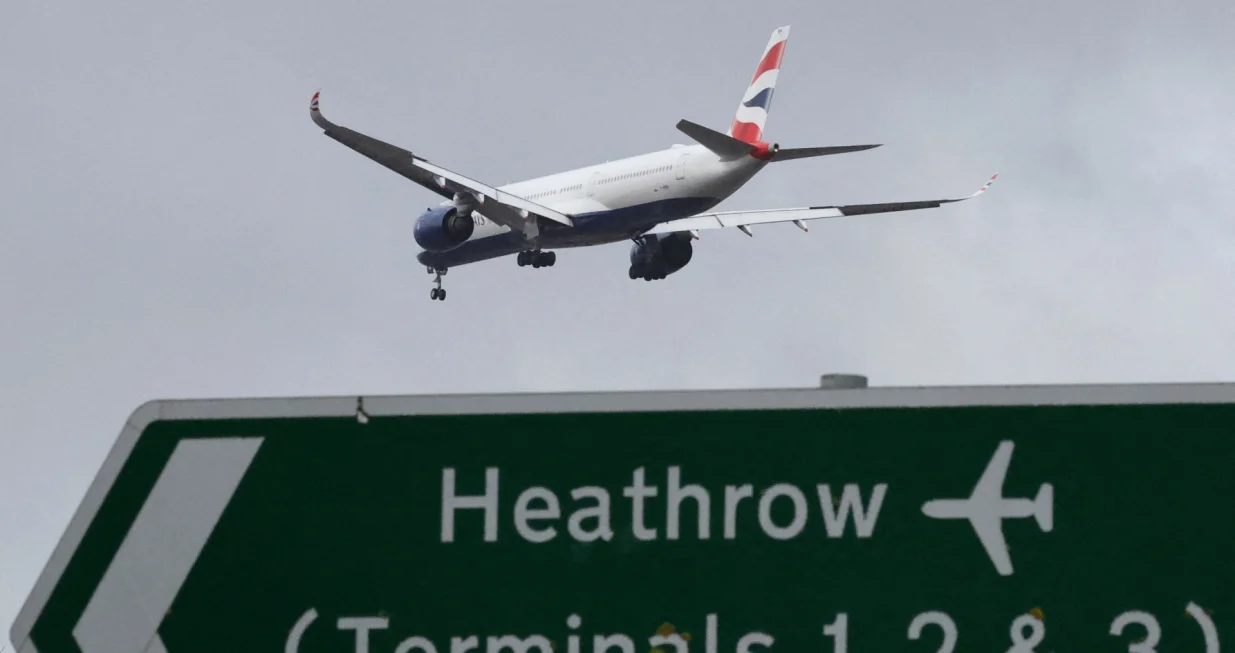 FILE PHOTO: A British Airways passenger plane flies over a road direction sign as it makes its landing approach to Heathrow Airport in west London, Britain, January 28, 2025. REUTERS/Toby Melville/File Photo/Toby Melville