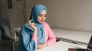 young pretty modern muslim woman in hijab working on laptop in office room, education online, remote work freelancer, making notes thinking, hidžab, posao, žena/Freepik