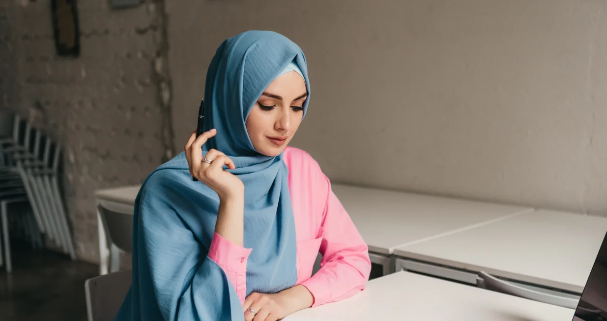 young pretty modern muslim woman in hijab working on laptop in office room, education online, remote work freelancer, making notes thinking, hidžab, posao, žena/Freepik