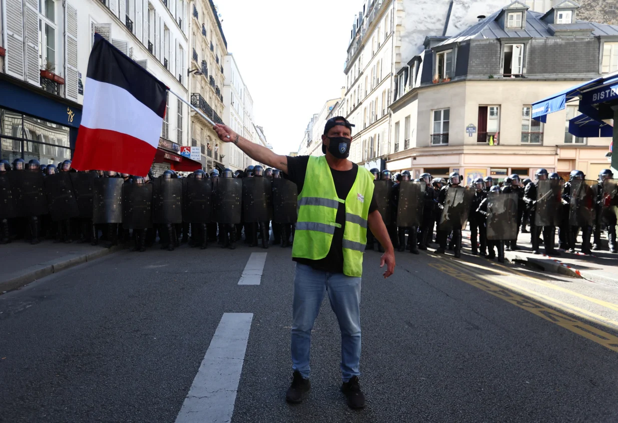 A protester wearing a yellow vest holds a French national flag in front of French CRS riot police during a demonstration in Paris as part of a day of nationwide strikes and protests against the government and cuts in the next budget, with supporters of the "Bloquons Tout" (Let's Block Everything) movement, France, September 18, 2025. REUTERS/Abdul Saboor/Abdul Saboor