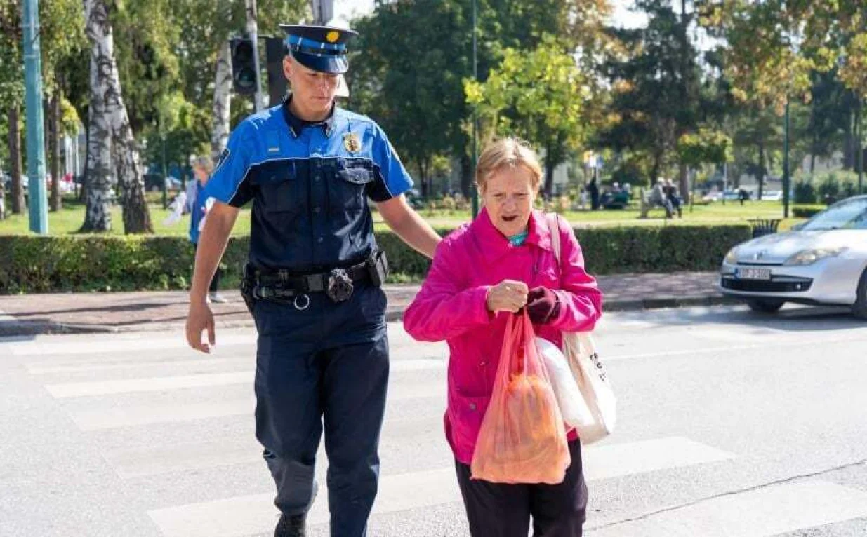 Policajac pomaže starijoj gospođi da pređe cestu/Mup Ks