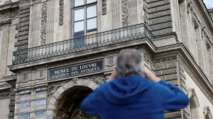 A man takes a picture of a broken window protected by a wooden panel at the Louvre Museum as the museum remains closed the day after a spectacular jewel heist by thieves who broke into the landmark by using a crane and smashing an upstairs window, stealing priceless jewelry from an area that houses the French crown jewels before escaping on motorbikes, in Paris, France, October 20, 2025. REUTERS/Benoit Tessier/Benoit Tessier