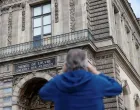 A man takes a picture of a broken window protected by a wooden panel at the Louvre Museum as the museum remains closed the day after a spectacular jewel heist by thieves who broke into the landmark by using a crane and smashing an upstairs window, stealing priceless jewelry from an area that houses the French crown jewels before escaping on motorbikes, in Paris, France, October 20, 2025. REUTERS/Benoit Tessier/Benoit Tessier