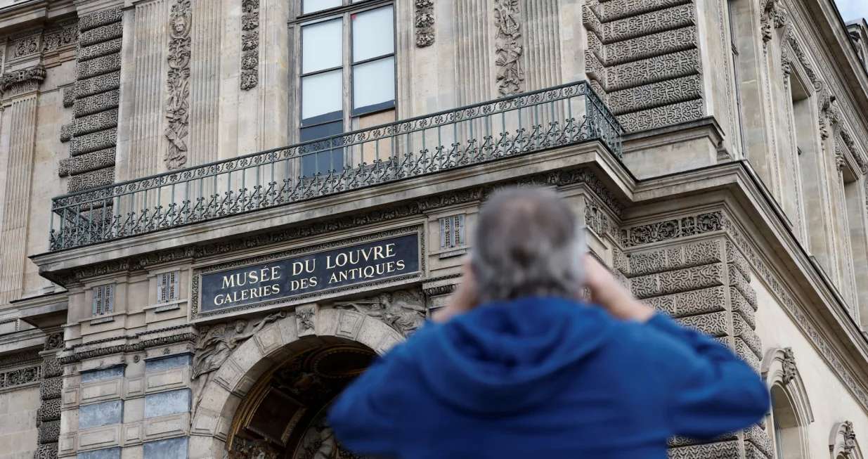 A man takes a picture of a broken window protected by a wooden panel at the Louvre Museum as the museum remains closed the day after a spectacular jewel heist by thieves who broke into the landmark by using a crane and smashing an upstairs window, stealing priceless jewelry from an area that houses the French crown jewels before escaping on motorbikes, in Paris, France, October 20, 2025. REUTERS/Benoit Tessier/Benoit Tessier