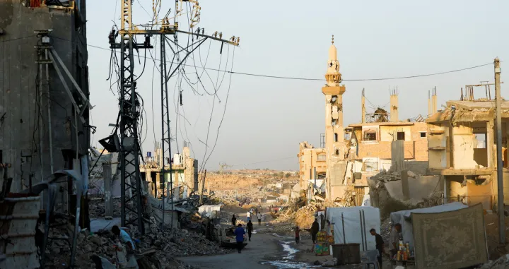 People walk past damaged electricity poles in Nuseirat, central Gaza Strip, October 31, 2025. REUTERS/Mahmoud Issa/Mahmoud Issa