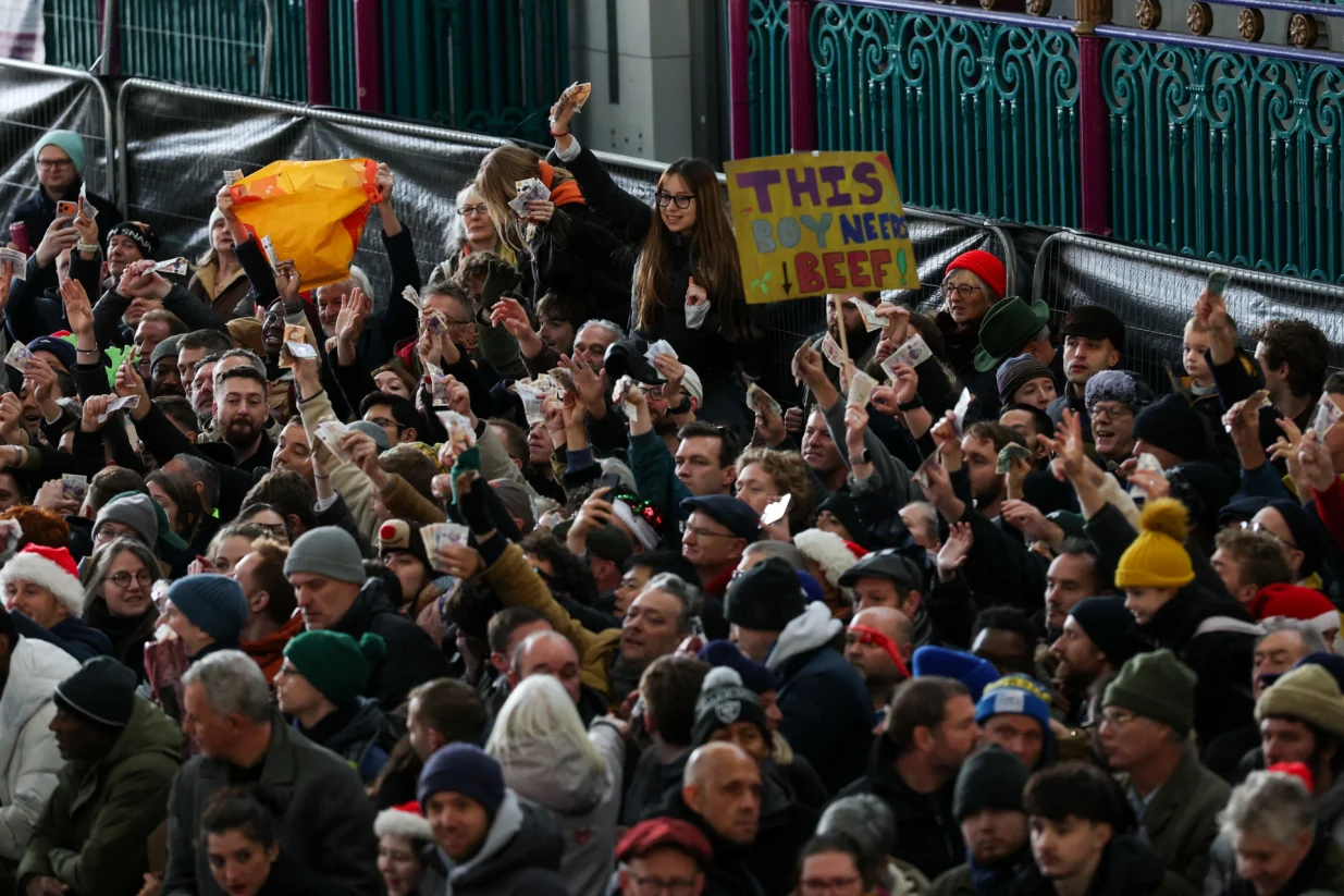 People in the crowd hold up banknotes as they shop for meat during a pre-Christmas auction in Smithfield Market in London, Britain, December 24, 2025. REUTERS/Isabel Infantes/Foto: Isabel Infantes