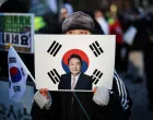 A woman holds a sign bearing South Korean national flag with a portrait of former President Yoon Suk Yeol, as they wait for his arrival for the final arguments in his insurrection trial, at a court in Seoul, South Korea, January 13, 2026. REUTERS/Kim Hong-Ji/Kim Hong-ji