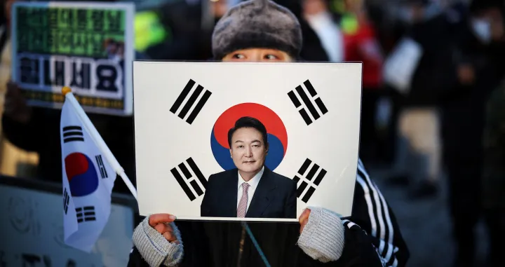 A woman holds a sign bearing South Korean national flag with a portrait of former President Yoon Suk Yeol, as they wait for his arrival for the final arguments in his insurrection trial, at a court in Seoul, South Korea, January 13, 2026. REUTERS/Kim Hong-Ji/Kim Hong-ji