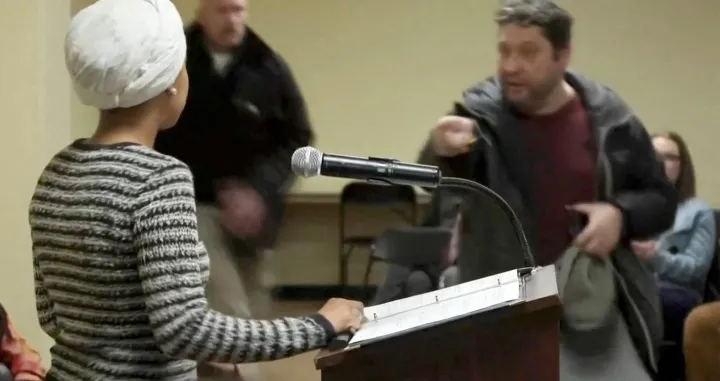 A man shouts at U.S. Representative Ilhan Omar (D-MN) after spraying an unidentified liquid in her direction, during a town hall meeting days after a man identified as Alex Pretti was fatally shot by federal immigration agents trying to detain him, in Minneapolis, Minnesota, U.S., January 27, 2026 in a still image from video. REUTERS/Maria Alejandra Cardona  TPX IMAGES OF THE DAY/Maria Alejandra Cardona