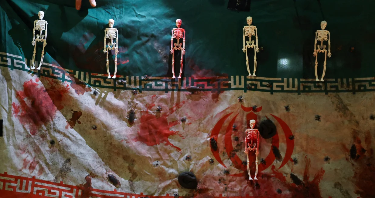 A hand touches an Iranian flag which is covered in fake blood, as well as skeleton and insect representations, as demonstrators attend a gathering outside the Iranian embassy in support of nationwide protests in Iran, in London, Britain, January 18, 2026. REUTERS/Toby Melville/Toby Melville