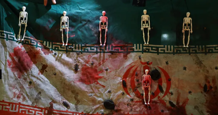 A hand touches an Iranian flag which is covered in fake blood, as well as skeleton and insect representations, as demonstrators attend a gathering outside the Iranian embassy in support of nationwide protests in Iran, in London, Britain, January 18, 2026. REUTERS/Toby Melville/Toby Melville