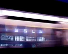 epa10387461 The Tesla logo seen through a window of a bus passing in front of the Tesla Gigafactory in Gruenheide near Berlin, Germany, 03 January 2023. The Tesla Gigafactory Berlin-Brandenburg plant in Gruenheide produces 2,000 Model Y electric cars in a week. EPA/Filip Singer/Filip Singer